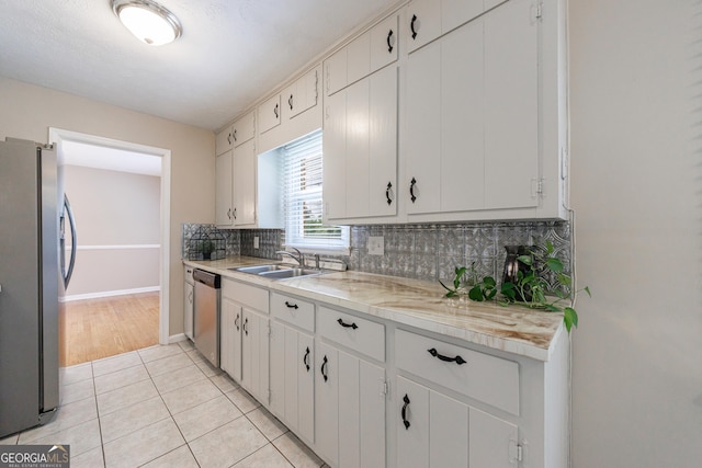 kitchen featuring appliances with stainless steel finishes, a sink, light countertops, light tile patterned floors, and tasteful backsplash