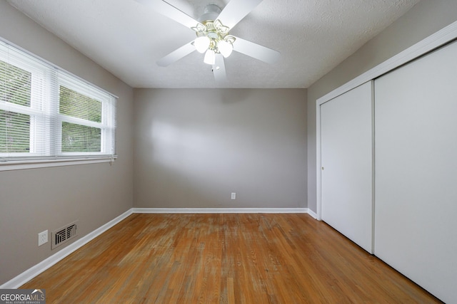 unfurnished bedroom featuring visible vents, a closet, wood finished floors, baseboards, and a ceiling fan
