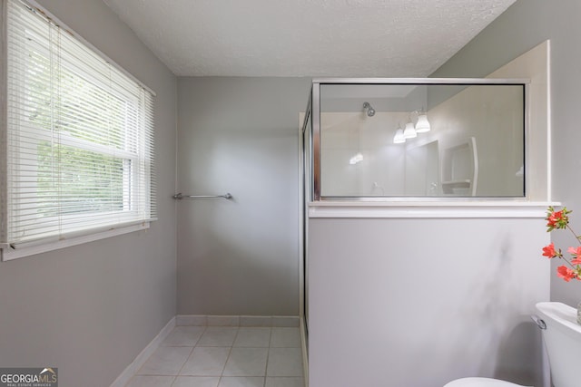 bathroom featuring a textured ceiling, tile patterned flooring, a stall shower, baseboards, and toilet