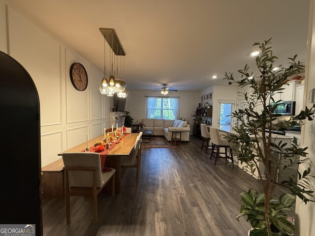 dining space with arched walkways, ceiling fan, dark wood-style floors, and a decorative wall