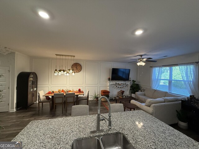 living room featuring ceiling fan, a decorative wall, and dark wood-type flooring