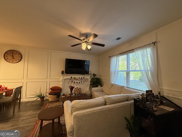 living area featuring visible vents, ceiling fan, a decorative wall, and wood finished floors