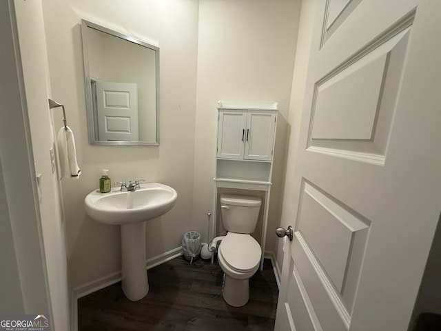 half bath with baseboards, a sink, wood finished floors, and toilet
