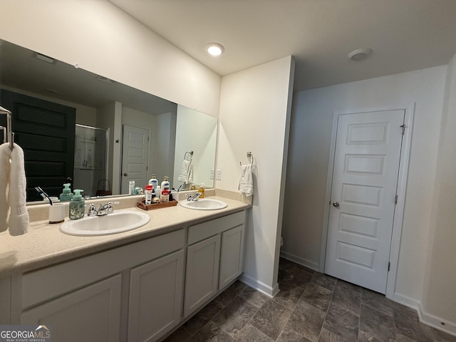 bathroom with double vanity, a sink, baseboards, and a shower stall