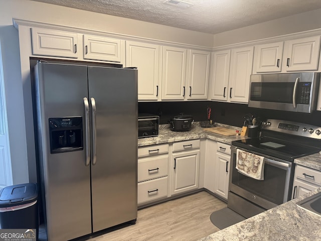 kitchen featuring a textured ceiling, a toaster, white cabinets, light wood finished floors, and stainless steel appliances