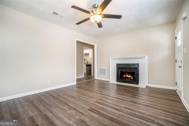 4004 Knightsbridge Rd, Kennesaw, GA 30144 - unfurnished living room with a brick fireplace, dark wood-style flooring, ceiling fan, and visible vents