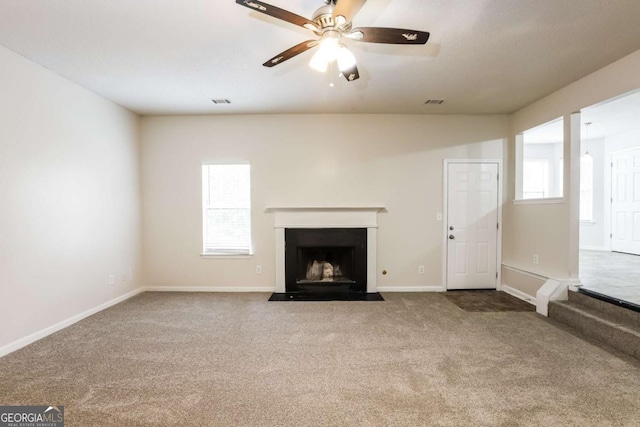 unfurnished living room with carpet flooring, a ceiling fan, baseboards, and a fireplace with flush hearth