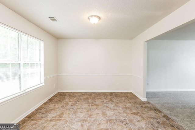 spare room featuring baseboards, visible vents, a textured ceiling, and a wealth of natural light