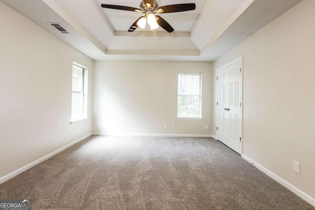carpeted empty room with visible vents, ceiling fan, a tray ceiling, and a wealth of natural light