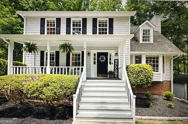 view of front of house featuring a chimney, covered porch, and a shingled roof