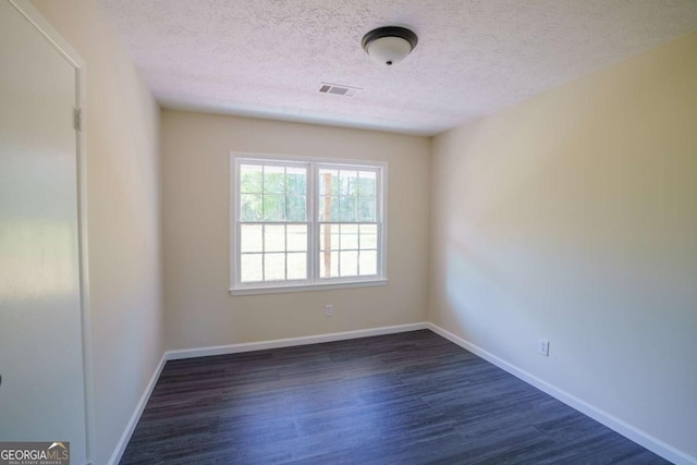 unfurnished room featuring baseboards, dark wood finished floors, a textured ceiling, and visible vents