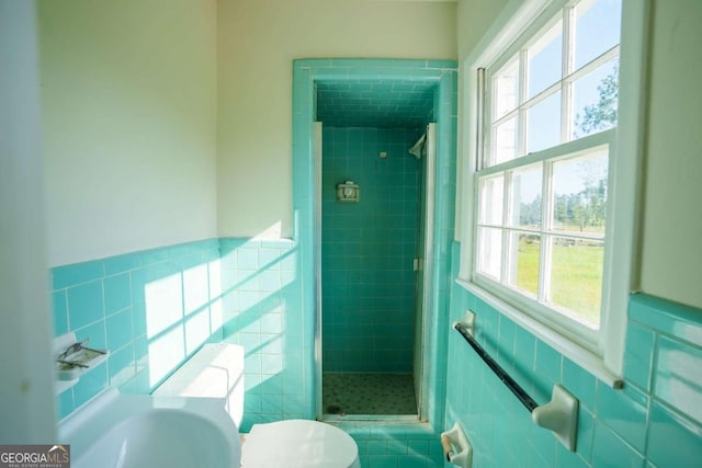 interior space featuring toilet, tile walls, wainscoting, and a stall shower