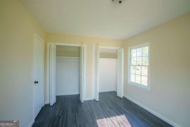 unfurnished bedroom featuring baseboards, two closets, and dark wood-style floors