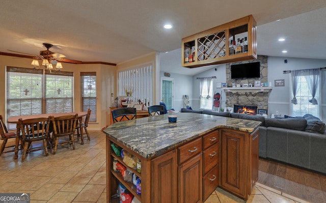 kitchen featuring a ceiling fan, open floor plan, a stone fireplace, and brown cabinetry