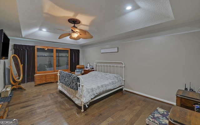 bedroom featuring a ceiling fan, a textured ceiling, wood finished floors, baseboards, and a tray ceiling