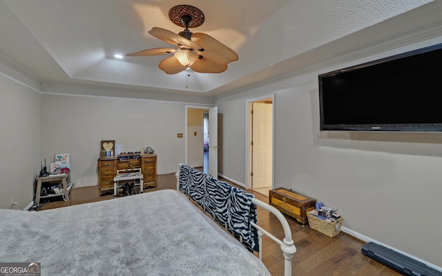 bedroom with wood finished floors, baseboards, a raised ceiling, a textured ceiling, and a ceiling fan