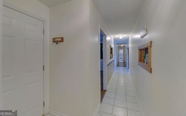 corridor featuring light tile patterned flooring, a textured ceiling, and baseboards