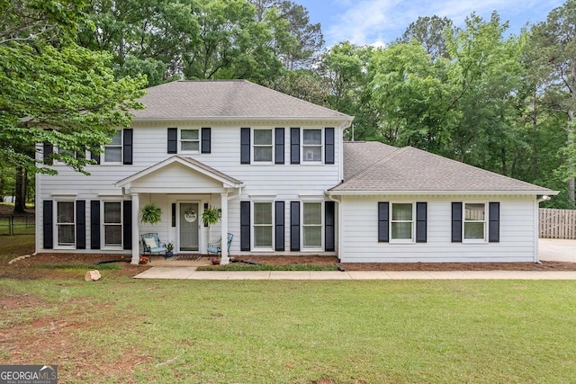colonial home featuring fence, a shingled roof, and a front yard