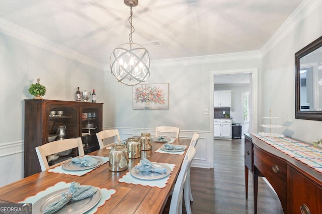 dining room featuring a notable chandelier, dark wood finished floors, a wainscoted wall, visible vents, and ornamental molding