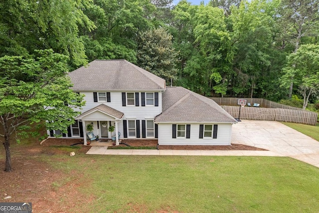 colonial-style house featuring a shingled roof, fence, covered porch, and a front yard