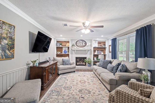 living room featuring ceiling fan, a brick fireplace, a textured ceiling, wood finished floors, and ornamental molding