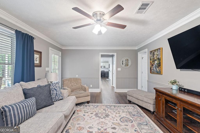 living area with ornamental molding, a ceiling fan, dark wood-type flooring, and visible vents