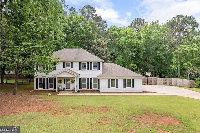 colonial-style house with a porch, fence, a shingled roof, and a front yard