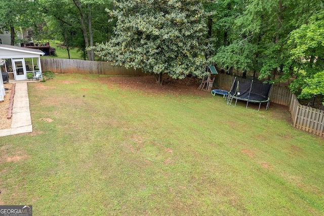 view of yard with a sunroom, a fenced backyard, and a trampoline