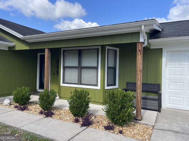 doorway to property with an attached garage, roof with shingles, and covered porch
