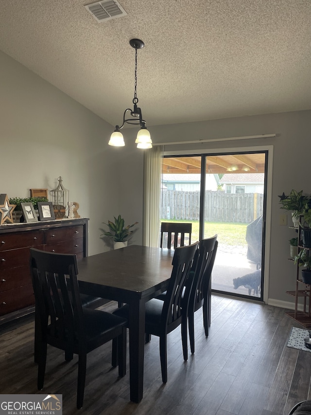 dining space featuring visible vents, a textured ceiling, dark wood finished floors, and vaulted ceiling