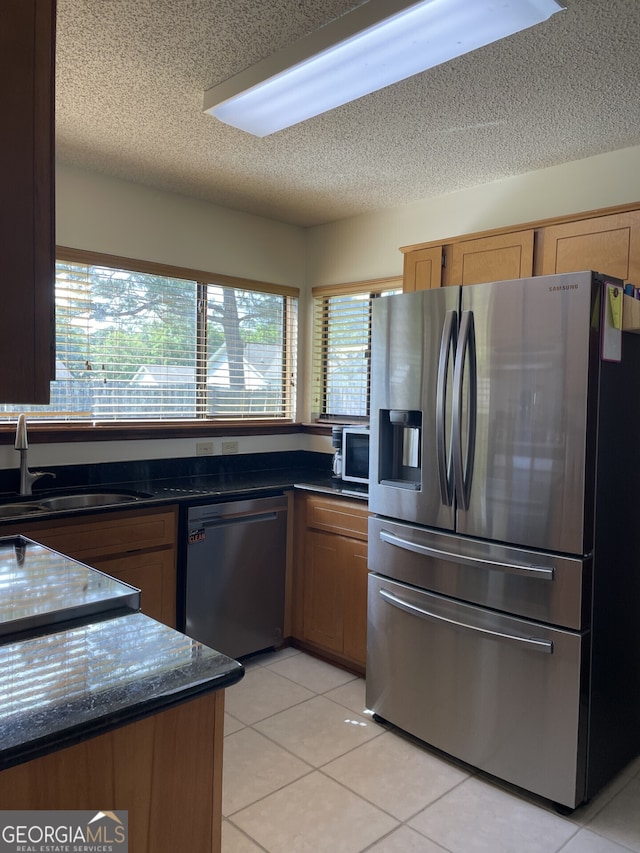 kitchen featuring a textured ceiling, appliances with stainless steel finishes, a sink, light tile patterned floors, and dark stone counters