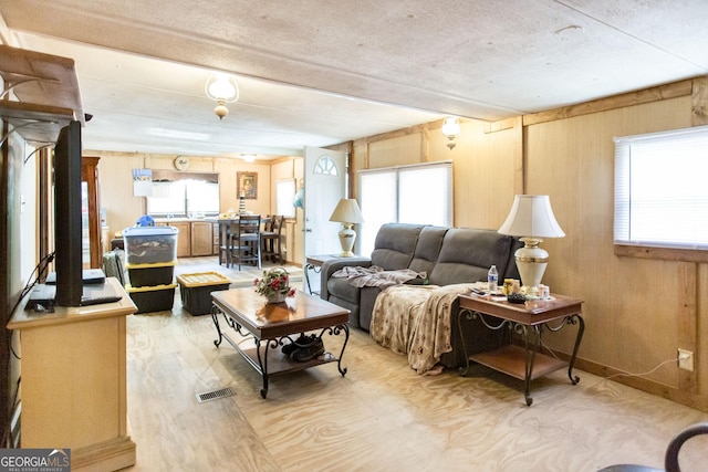living room featuring visible vents, beam ceiling, wooden walls, and light wood-type flooring
