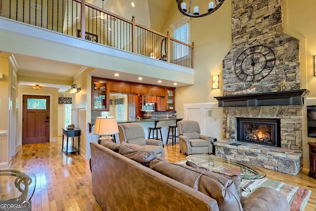 living room featuring a high ceiling, light wood finished floors, a fireplace, a chandelier, and ornamental molding
