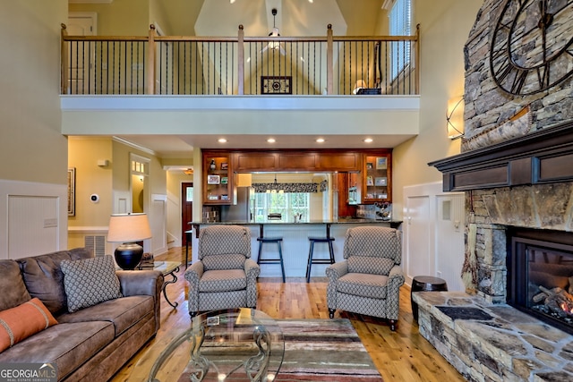 living room with ornamental molding, a stone fireplace, wood finished floors, and a towering ceiling