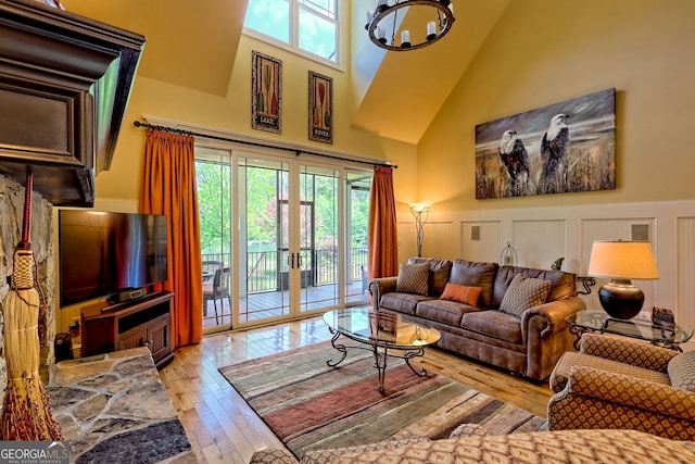 living room with french doors, a towering ceiling, a wainscoted wall, a decorative wall, and hardwood / wood-style floors