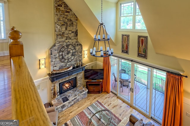living room featuring high vaulted ceiling, a chandelier, a stone fireplace, and wood finished floors