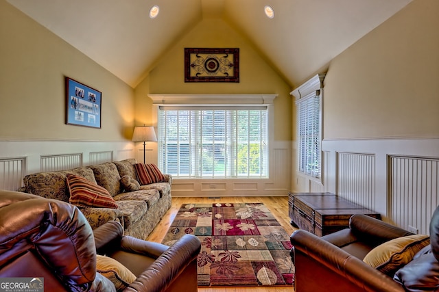 living room with lofted ceiling, wood finished floors, a decorative wall, and a wainscoted wall