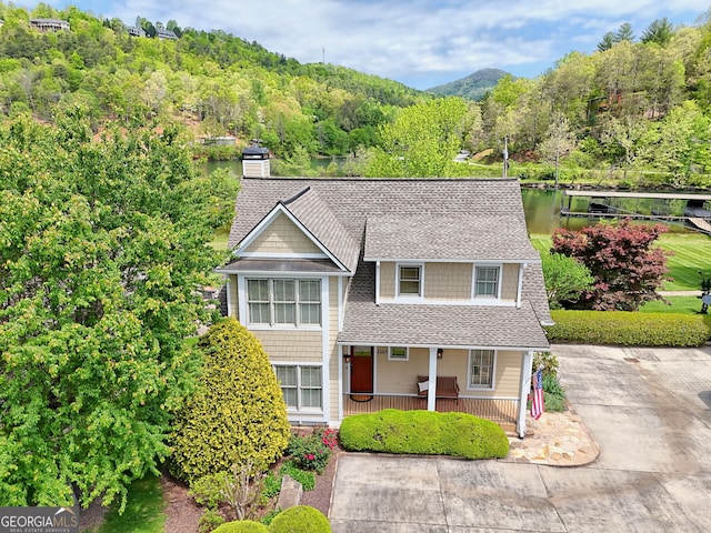 view of front of property with covered porch, roof with shingles, a chimney, a view of trees, and a mountain view