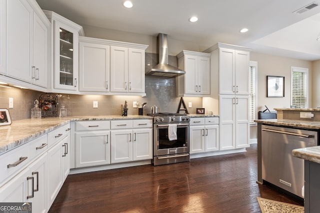 kitchen with appliances with stainless steel finishes, white cabinets, wall chimney exhaust hood, and visible vents
