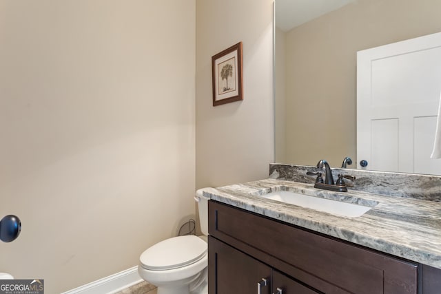 half bathroom featuring toilet, baseboards, and vanity