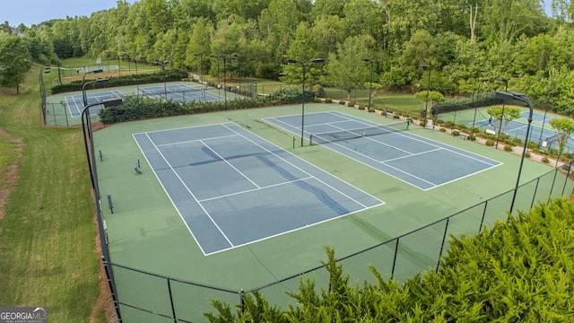 view of tennis court with fence and a forest view