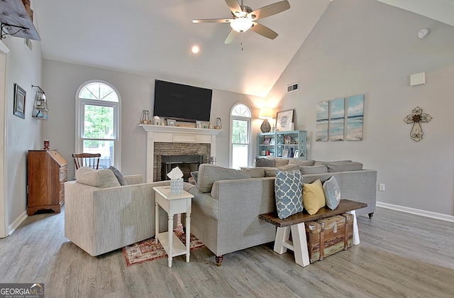 living area with ceiling fan, visible vents, a fireplace, light wood-type flooring, and high vaulted ceiling