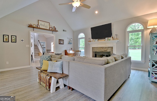 living area featuring visible vents, a stone fireplace, ceiling fan, high vaulted ceiling, and light wood finished floors