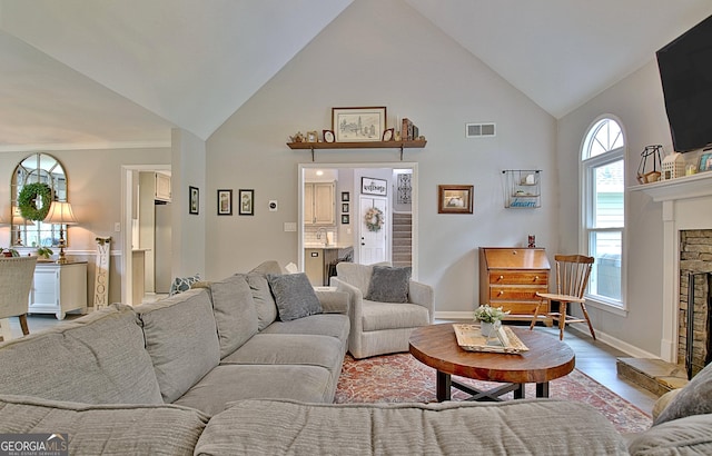 living room featuring visible vents, wood finished floors, high vaulted ceiling, baseboards, and a fireplace with raised hearth