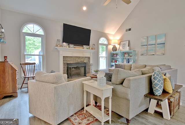 living area featuring ceiling fan, visible vents, a fireplace, light wood-type flooring, and high vaulted ceiling