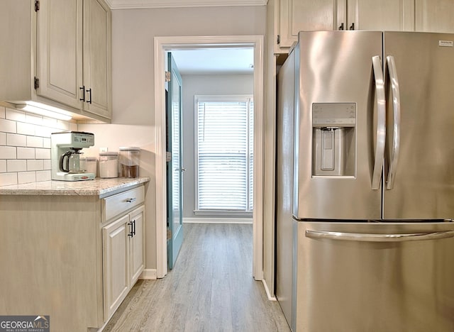 kitchen featuring decorative backsplash, baseboards, stainless steel fridge, light stone counters, and light wood finished floors