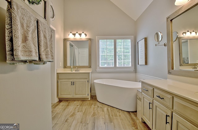 full bath featuring a freestanding tub, wood finished floors, two vanities, a sink, and lofted ceiling