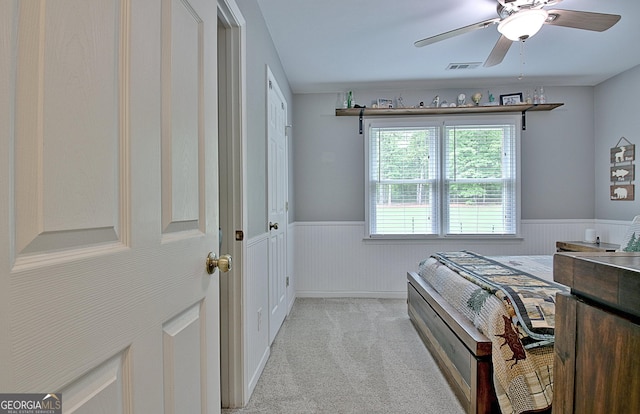 bedroom with a ceiling fan, light colored carpet, visible vents, and a wainscoted wall