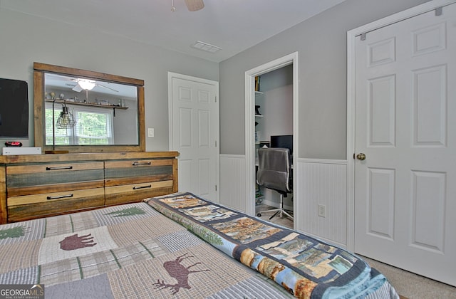 carpeted bedroom with a ceiling fan, visible vents, and wainscoting