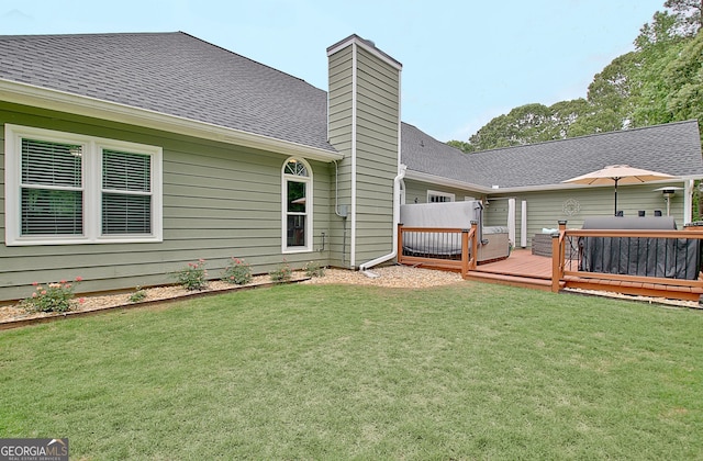 rear view of house with a lawn, roof with shingles, a wooden deck, and a chimney